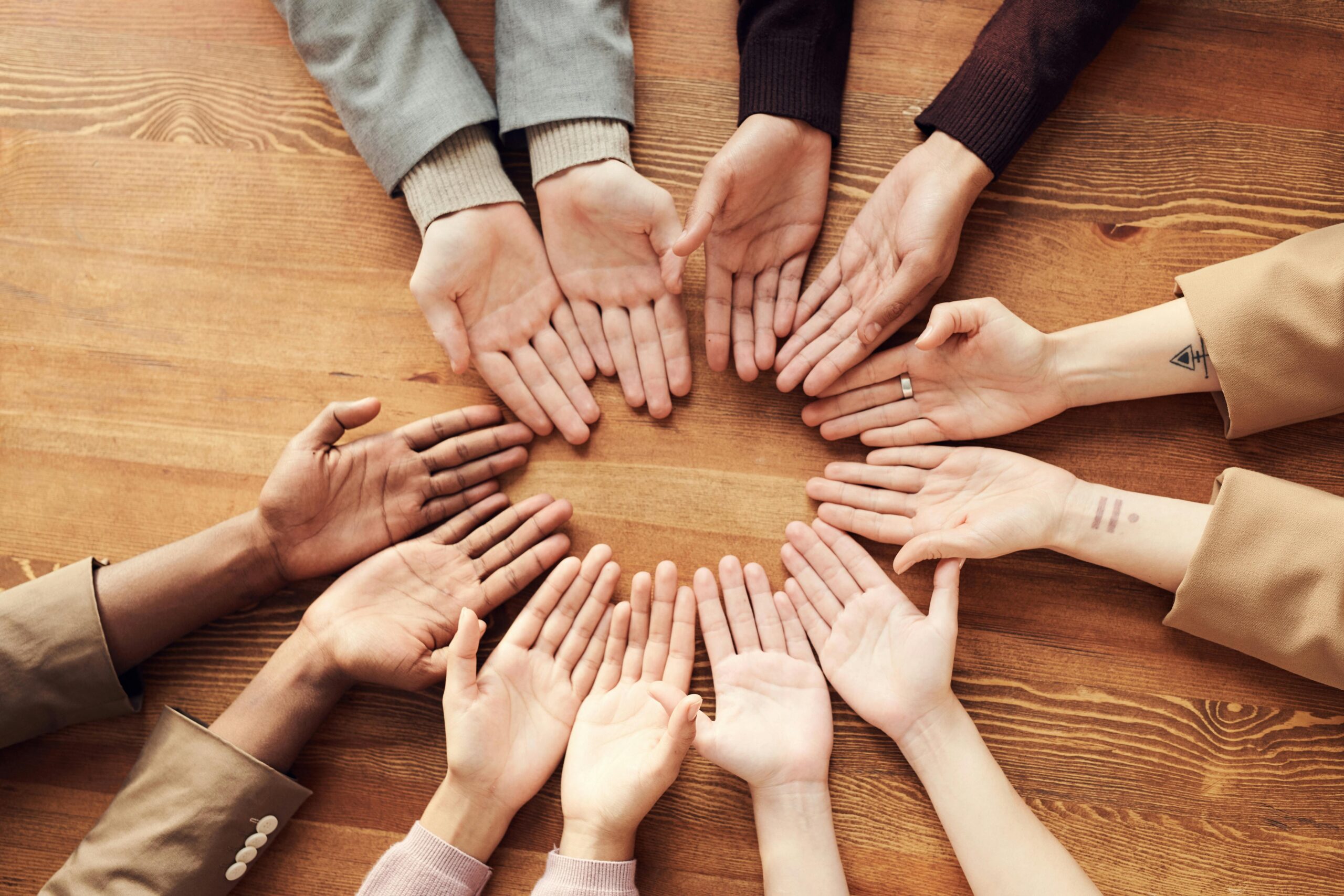 Top view of diverse hands forming a circle on a wooden table, symbolizing unity and diversity.