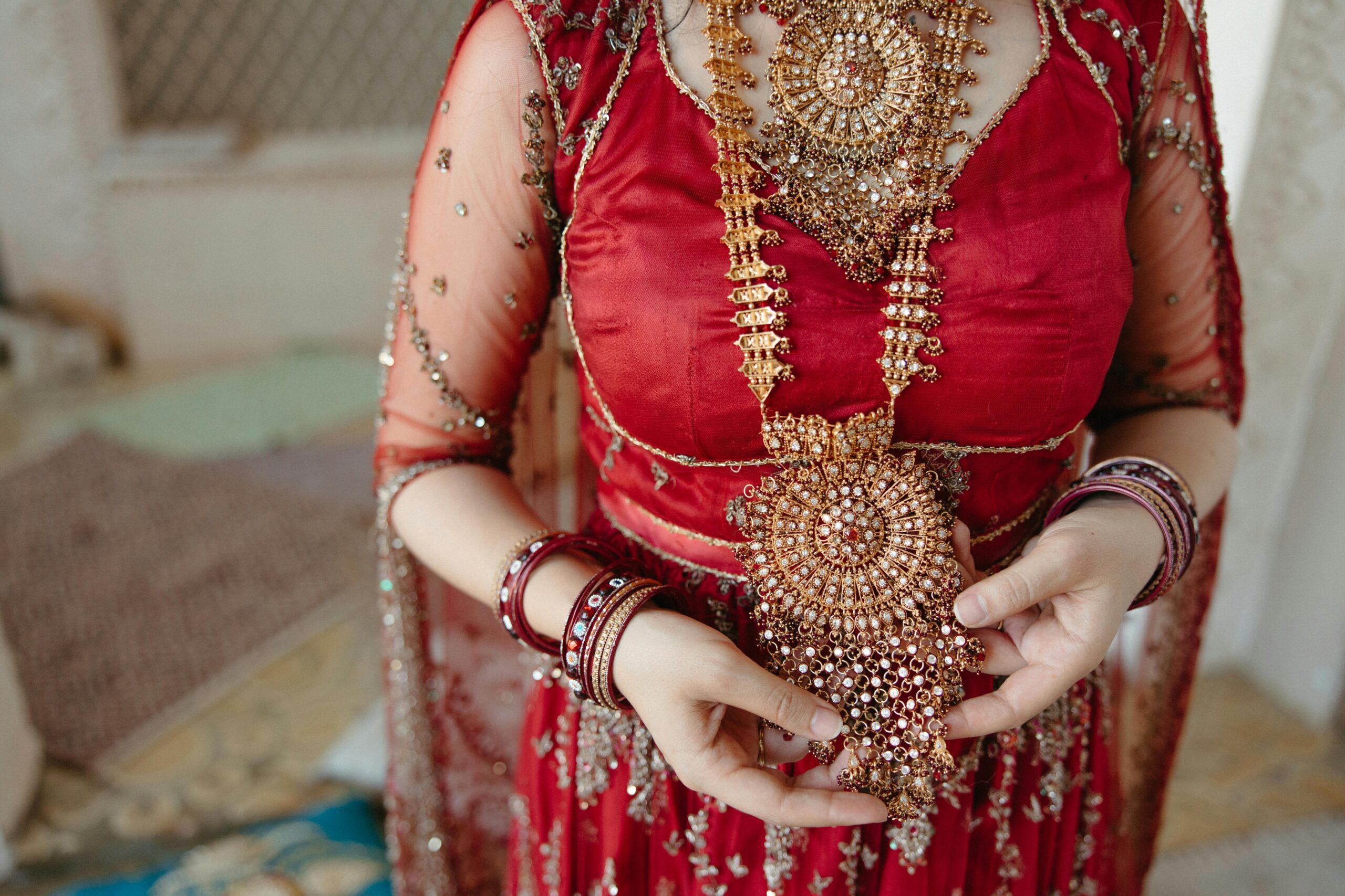 Close-up of traditional bridal jewelry and red sari, showcasing intricate craftsmanship and style.